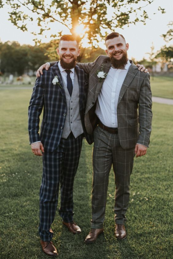 a groom and groomsman wearing plaid and windowpane print suits, white shirts and white floral boutonnieres look cool