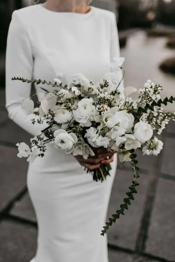a minimalist winter bridal look with a plain fitting wedding dress with a high neckline and long sleeves plus a white ranunculus wedding bouquet