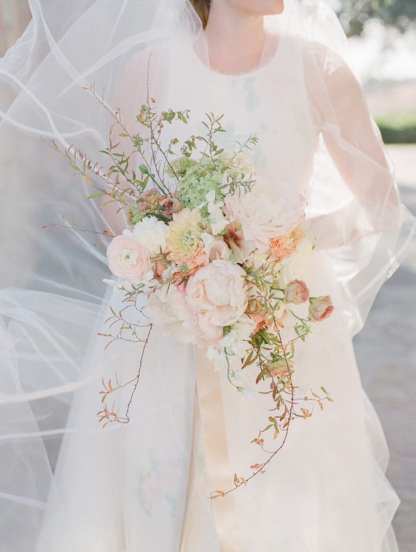 a unique S shaped bouquet with delicately colored blooms, greenery and some twigs is a refined and chic solution for a wedding