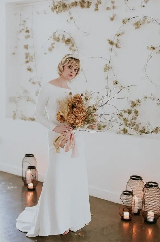 a minimalist winter bridal outfit with a white plain A line wedding dress with a bateau neckline and long sleeves, a train and a headpiece with a veil