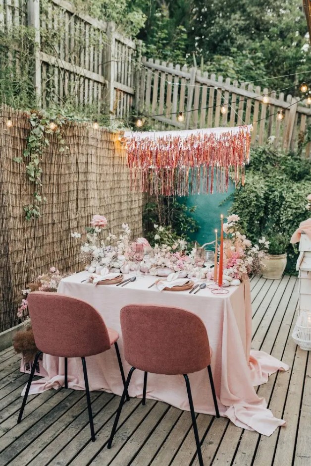 a little pink reception space right on the terrace of the house, with lush blooms, shiny fringe and candles
