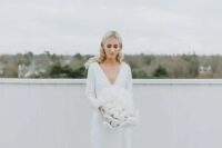17 a pretty and simple minimalist winter bridal look with a plain wedding dress with a deep V-neckline, long sleeves and a train plus a lush white wedding bouquet
