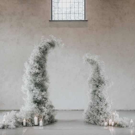 a delicate winter wedding altar compose of white baby's breath and pillar candles catches an eye with its shape