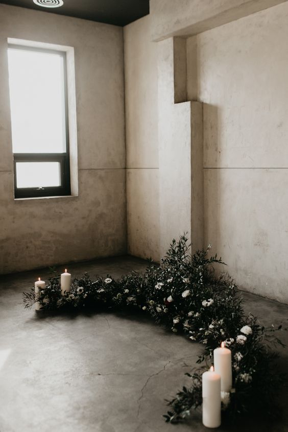 a winter wedding altar of greenery and white blooms and pillar candles is a stylish and cool idea for a minimalist wedding