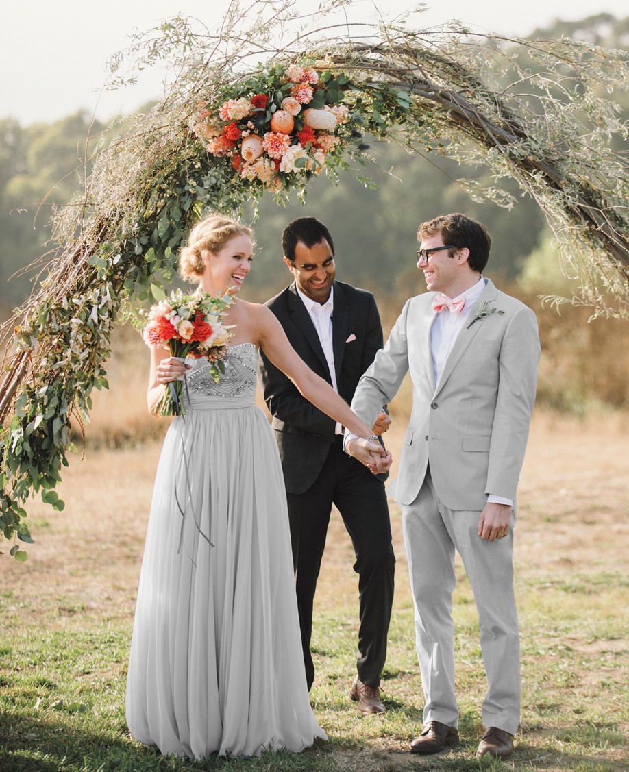 a creative wedding arch formed from willow branches, topped with greenery and a bold floral arrangement is a unique idea