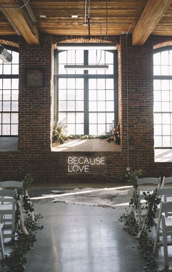 a minimalist winter ceremony space with white blooms and greenery, neon and an animal skin, greenery on the chairs
