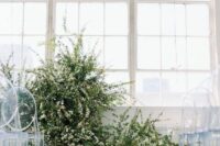 25 a minimalist winter wedding ceremony space done with greenery and white blooms, pillar candles and clear chairs
