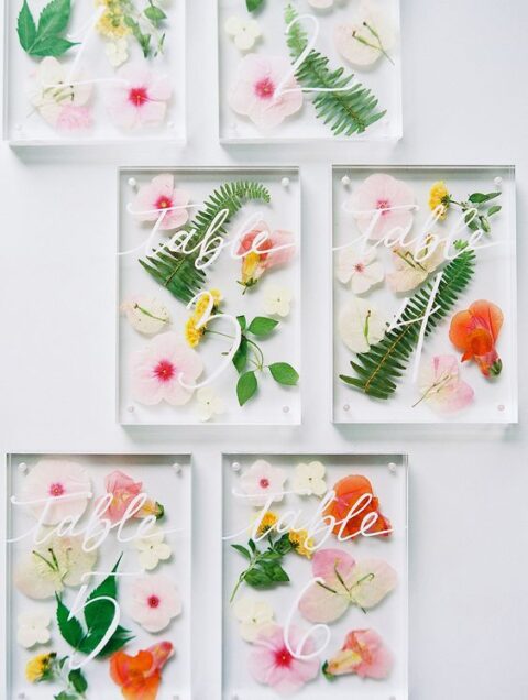 super cool and bright pressed flower and leaf wedding table numbers with white calligraphy are gorgeous
