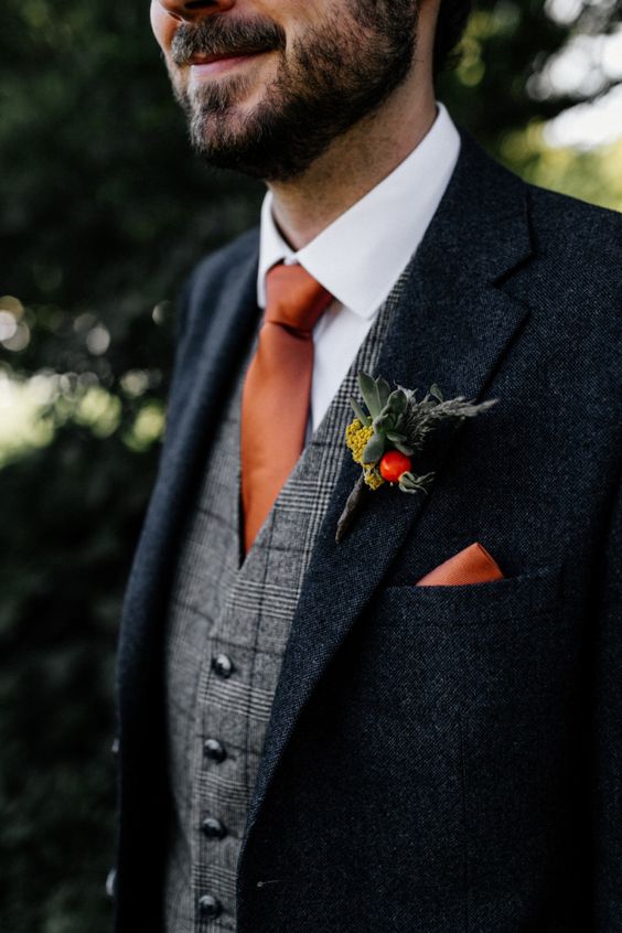 a black tweed suit, a grey plaid waistcoat, an orange tie and a handkerchief, a bold boutonniere are a lovely fall or winter groom's look