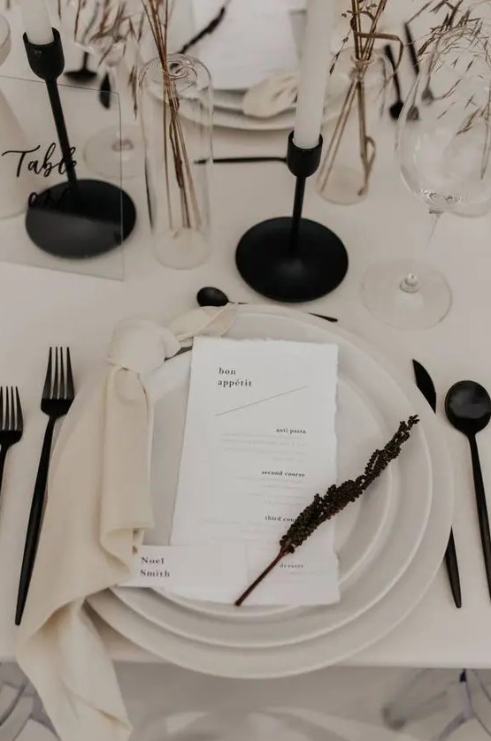 a contrasting minimalist wedding tablescape with neutral plates, black cutlery candlesticks and dried blooms and grasses