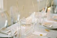 29 a delicate minimalist wedding tablescape with a grey tablecloth and napkins, white chargers and cutlery, some grasses in vases and tall and thin candles