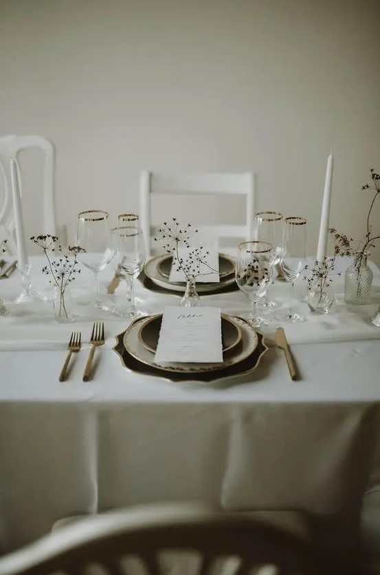 a dreamy and airy minimalist winter wedding tablescape with neutral linens, dried branches and blooms, black and white plates and dark cutlery