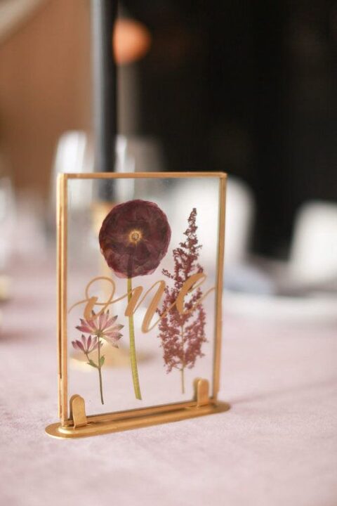 a lovely pressed flower wedding table number with a gold frame and gold calligraphy is a very pretty idea