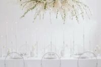 33 a minimalist ethereal wedding reception space with an oversized overhead floral decoration, sheer chairs and everything white