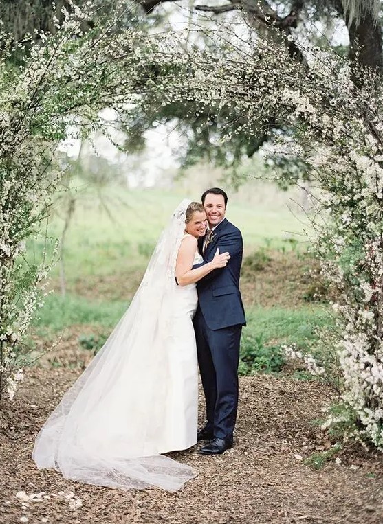 a romantic spring garden wedding arch covered with greenery and blooming branches looks fabulous and screams blooming and love