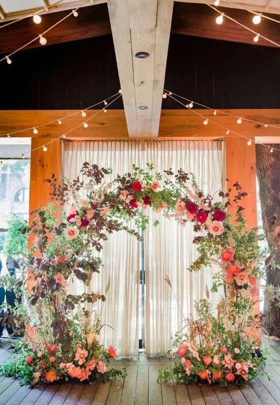 a round secret garden wedding arch covered with greenery, dark foliage, pink, blush and red blooms is a fabulous and bold idea for fall