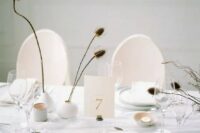 35 a minimalist neutral wedding tablescape with round white vases, dried branches and blooms, candles, white plates and chargers and a linen tablecloth
