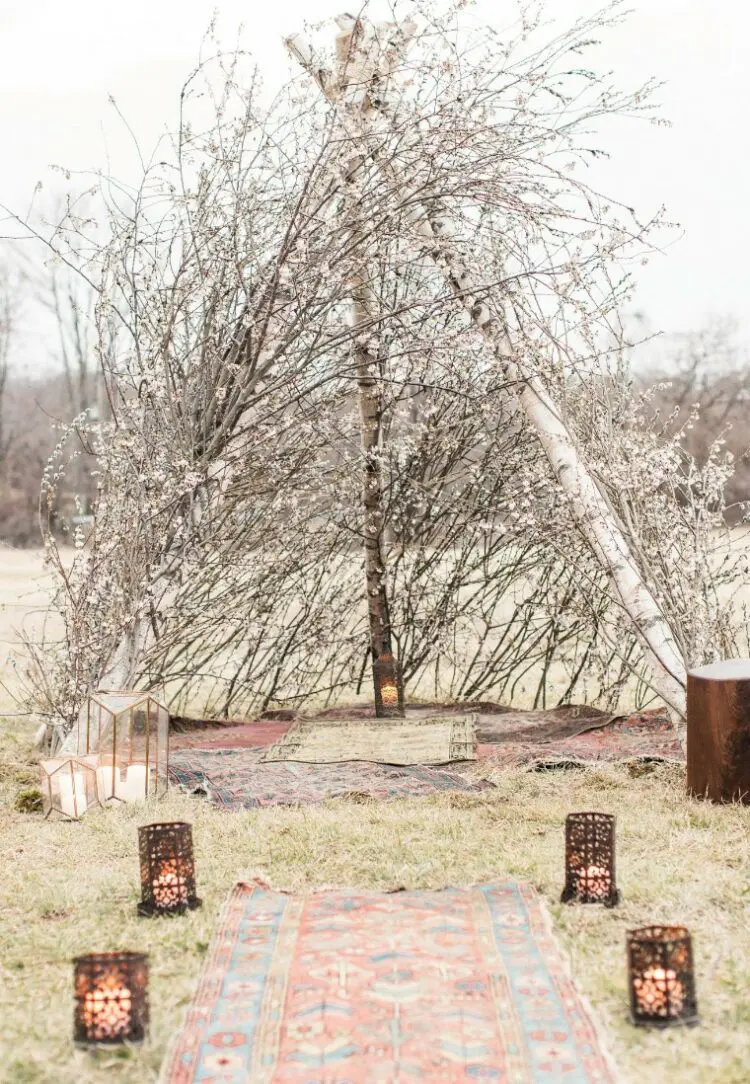 a triangle boho wedding altar made of blooming branches looks like a teepee, especially with boho rugs and candle lanterns