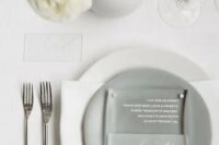 39 a neutral minimalist wedding table setting with white linens, a grey plate, white blooms in a round vase and simple cutlery