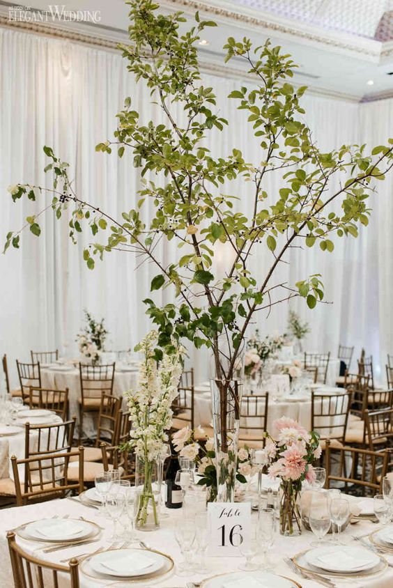 a cluster wedding centerpiece of white and blush blooms, greenery and branches is a cool solution for a wedding