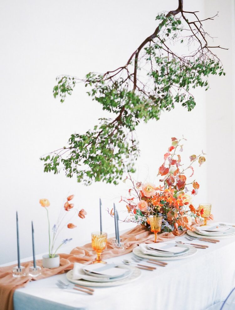 a creatively suspended greenery branch over the table elevates the whole tablescape and adds freshness to the orange and rust table decor