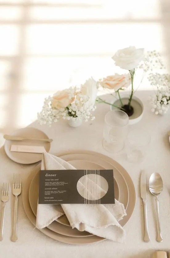a neutral winter wedding place setting with white and blush roses and baby's breath, neutral plates and simple modern cutlery