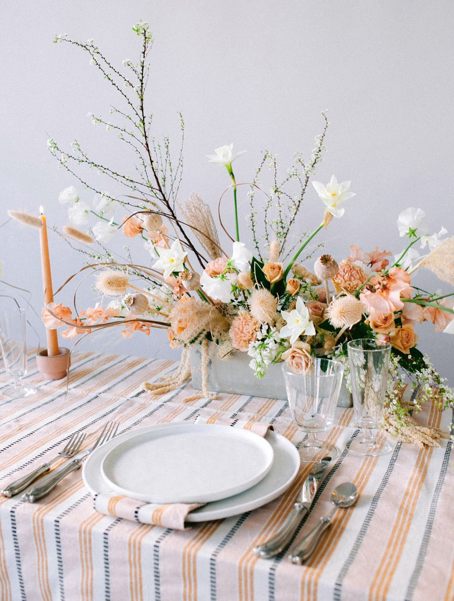 a gorgeous lush wedding centerpiece of white and orange blooms, dried ones, greenery and blooming branches and twigs