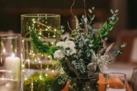 45 a lovely cluster wedding centerpiece of a jar with greenery and white blooms, a jar with moss and lights and candles around