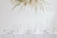 46 a minimalist ethereal wedding reception space with an oversized overhead floral decoration, sheer chairs and everything white
