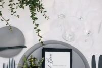 48 a stylish minimalist winter wedding tablescape with greenery, candles, matte grey plates, a black napkin