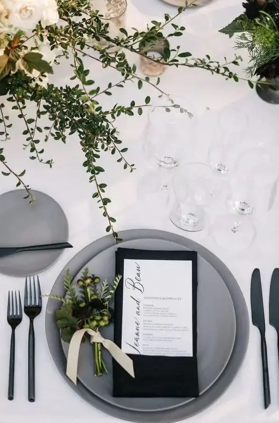 a stylish minimalist winter wedding tablescape with greenery, candles, matte grey plates, a black napkin