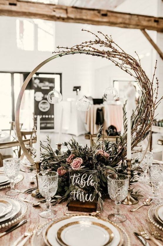 a romantic hoop wedding centerpiece with textural greenery, pink blooms and twigs going up the hoop plus a table number
