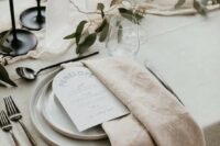 49 a stylish neutral wedding tablescape with a minimalist feel, with neutral plates and textural linens, greenery, blue candles and acrylic table numbers