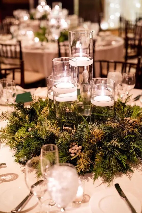 a beautiful woodland wedding centerpiece of evergreens and berries and tall glasses with floating candles is cool