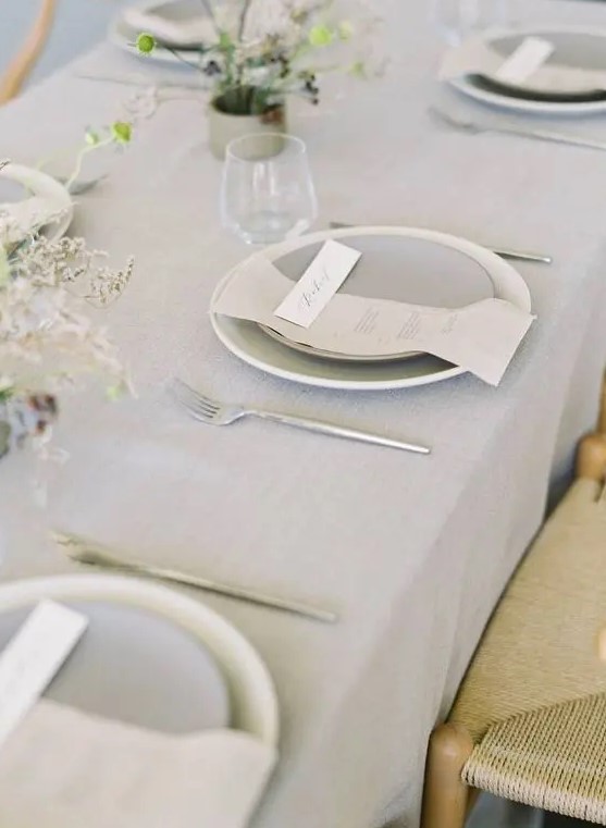 an airy minimalist wedding tablescape with a grey tablecloth, plates and napkins, dried blooms and candles is a stylish idea