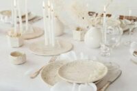 51 an airy white winter wedding tablescape with speckled plates, tall and thin white candles, dried branches with leaves and neutral linens