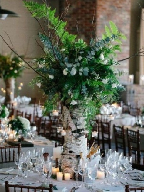 a woodland wedding centerpiece of a tree stump, white blooms, greenery and candle holders hanging on branches
