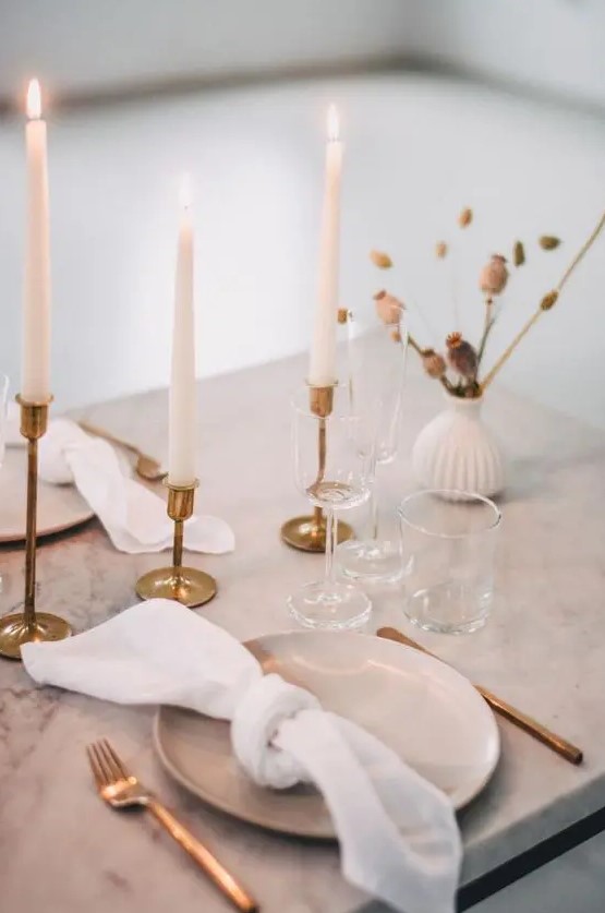 an elegant minimalist wedding tablescape with a marble table, tall and thin candles, dried blooms, gold cutlery and gold candlesticks