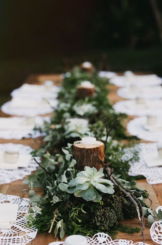 a simple woodland wedding tablescape with a runner made of moss, greenery, succulents and tree branches with candles