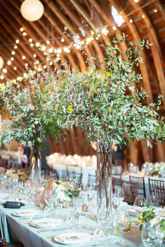 tall wedding centerpieces of greenery branches and some additional greenery on the table for a botanical feel
