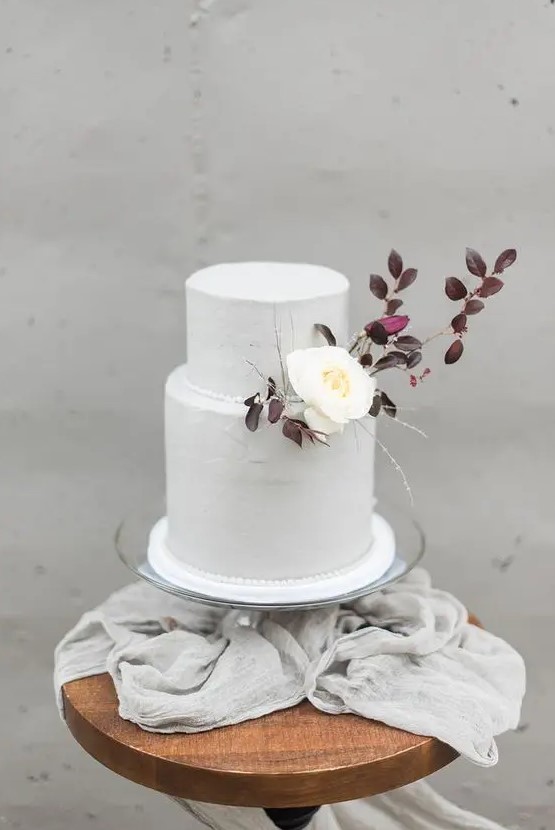 a purely white wedding cake decorated with dark foliage and a single white blooms for an early fall wedding with a Nordic twist