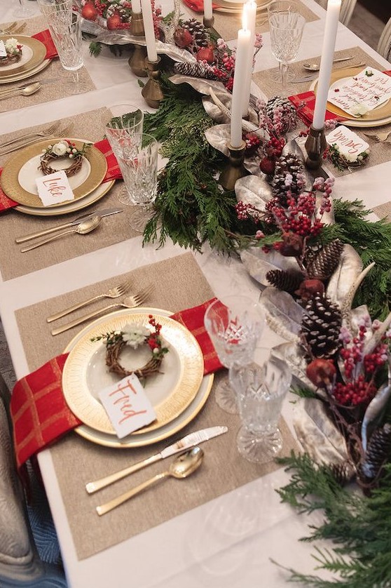 a Christmas wedding table setting with an evergreen, pinecone and berry runner, thin candles, red napkins and mini wreaths for place settings