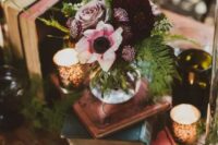 a beautiful dark enchanted forest wedding centerpiece of a stack of books, candles, a dark floral centerpiece and fern