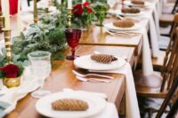 a beautiful winter wedding table with an evergreen runner, red glasses and blooms, pinecones and white porcelain