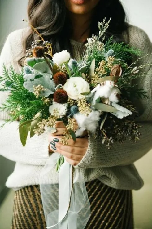 a boho winter wedding bouquet with much greenery, grasses, ferns, thistles and cotton