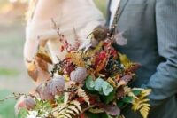 a bold woodland wedding bouquet with greenery, bold fall leaves, privet berries and long colorful ribbons