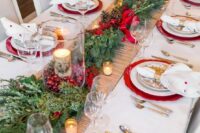 a bright Christmas wedding table with red chargers, an evergreen and pinecone runner, cranberries and birch bark candles, printed plates and polka dot napkins