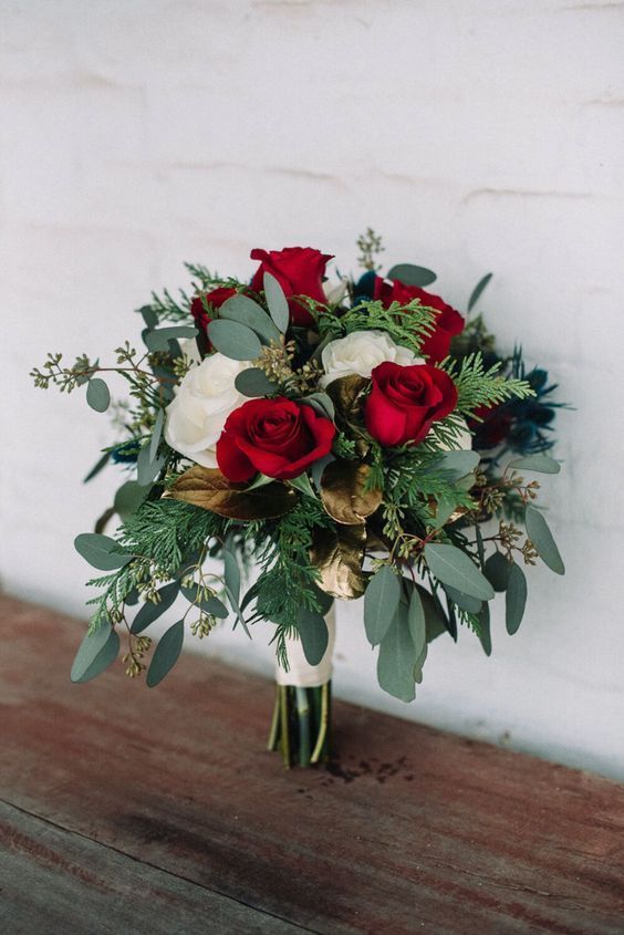 a bright wedding bouquet of white and red roses, greenery, evergreens, gold leaves and a white wrap is great for Christmas