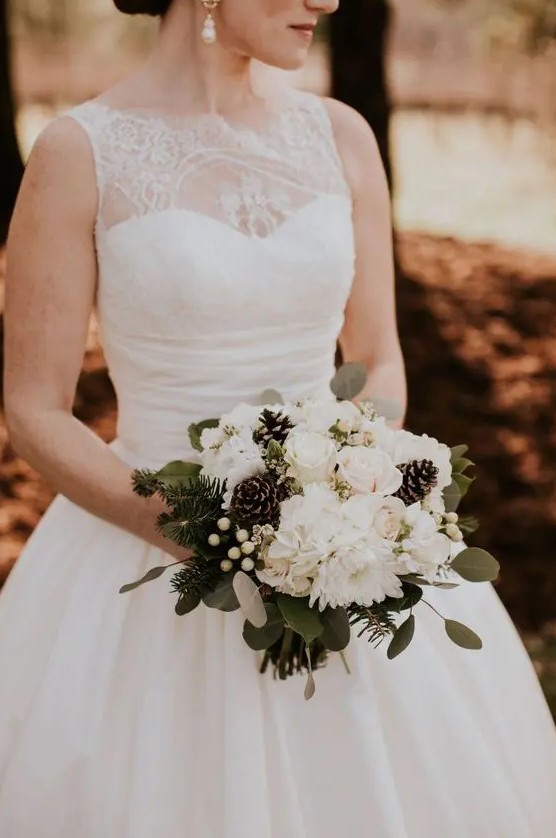 a chic winter wedding bouquet of white blooms, greenery, evergreens, berries and pinecones is a traditional idea for an elegant winter wedding