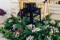 a classy winter wedding centerpiece of evergreens, baby’s breath, pinecones and a candle lantern in the center is amazing